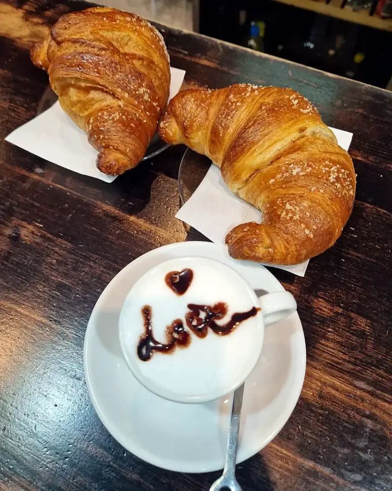 Due cornetti zuccherati su tovaglioli e un cappuccino con un cuore disegnato nella schiuma, sul banco di legno