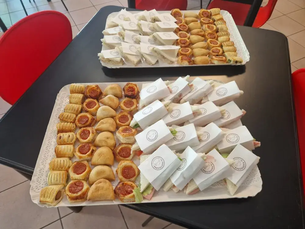 Due vassoi di rustici, pizzette e tramezzini incartati, pronti per il ritiro