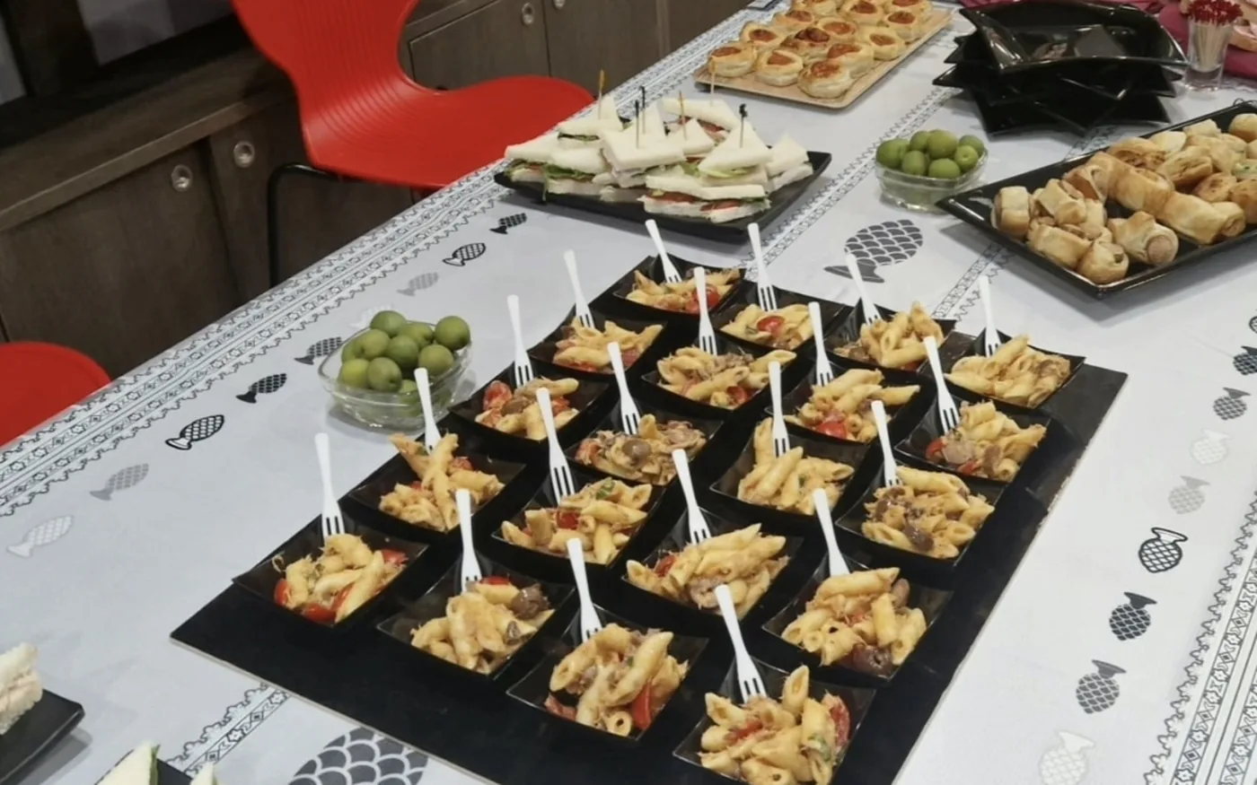 Vaschette di pasta fredda con la forchetta, tramezzini e rustici su una tavolata apparecchiata al bar