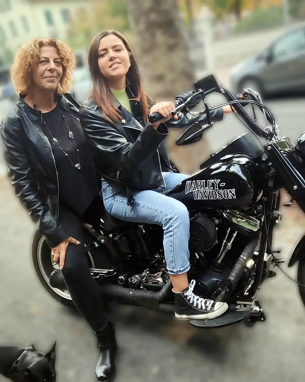 Desirée e Michela in giacca di pelle, sedute su una Harley-Davidson nera davanti al bar